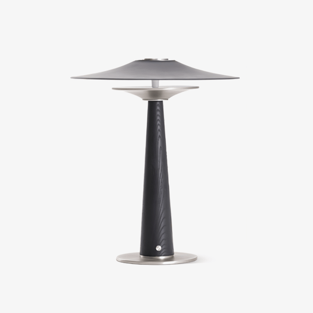 Bedroom table lamp with a wide disc on a black wood column, plain ground