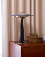Bedroom table lamp lit on a chest in front of a pale curtain