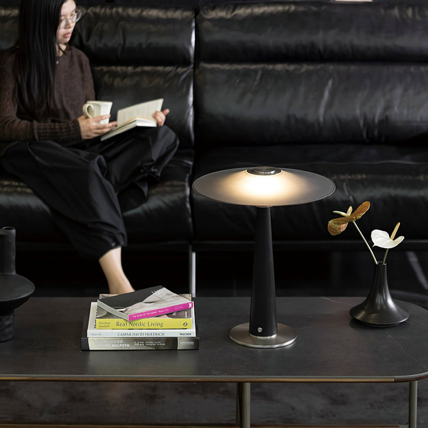 Bedroom table lamp lit on a table in front of a black leather sofa