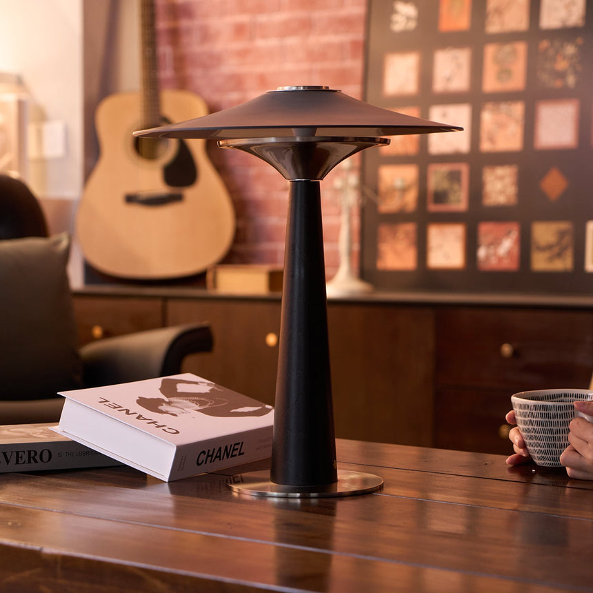 Bedroom table lamp lit on a wooden desk in a room with a guitar