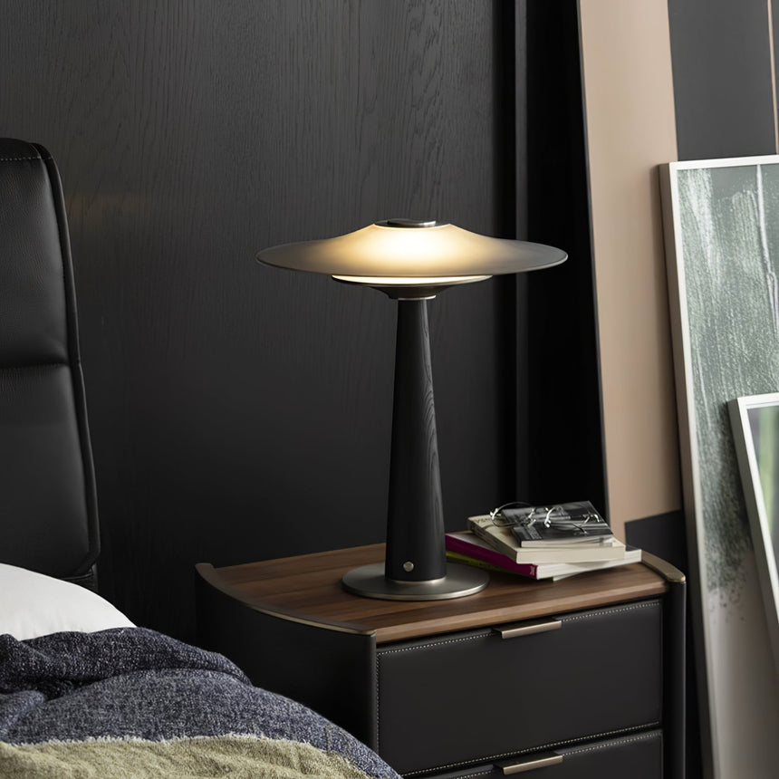 Bedroom table lamp lit on a dark nightstand beside a bed