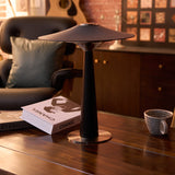 Bedroom table lamp lit on a wooden desk beside a mug and a book