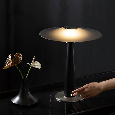 A hand touching the column of the lit bedroom table lamp on a dark table