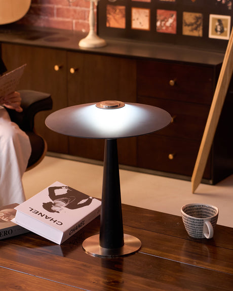 Bedroom table lamp lit on a desk beside a mirror and a magazine