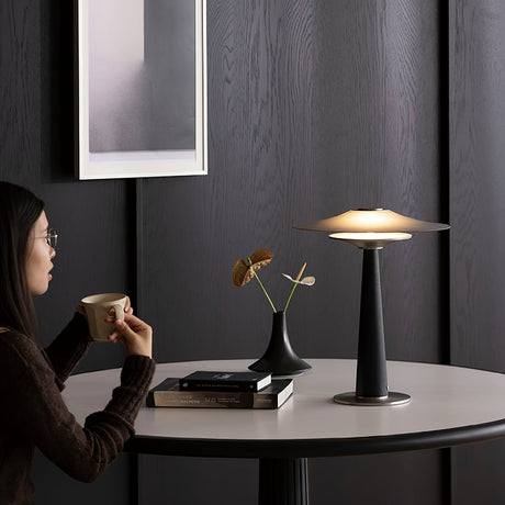 Bedroom table lamp lit on a table beside someone holding a cup