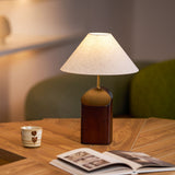 Bedroom table lamp lit on a wooden table beside a mug and a magazine