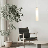 A white tube pendant lit beside an armchair and a large plant