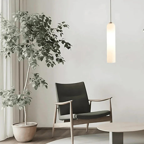 A white tube pendant lit beside an armchair and a large plant