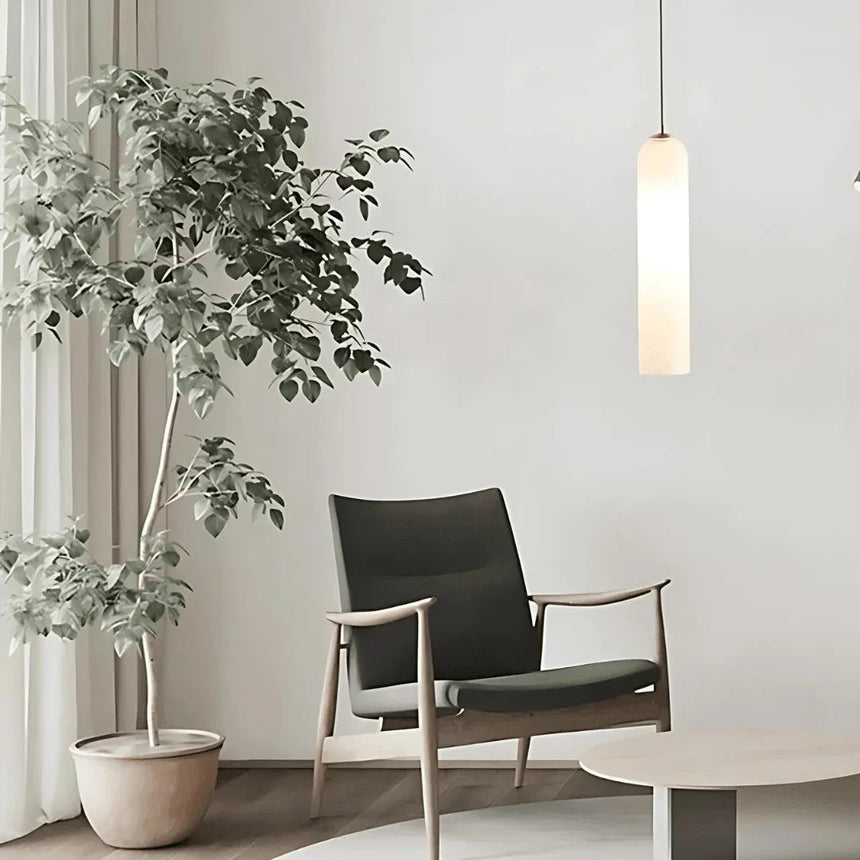 A white tube pendant lit beside an armchair and a large plant