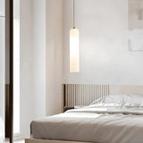 A white glass tube pendant lit beside a bed with a wooden headboard