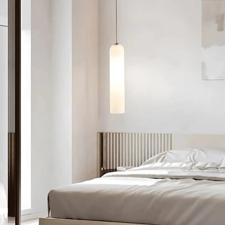 A white glass tube pendant lit beside a bed with a wooden headboard