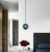 Deep green sphere lit in a hallway above a vase of red flowers