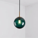 Deep green glass sphere with a brass holder and a lit bulb inside