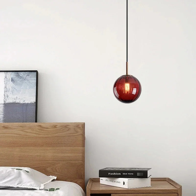 Small red glass sphere hanging low beside a bed over a wooden nightstand