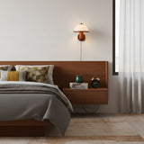 Oak wall lamp lit above a floating nightstand beside a made bed