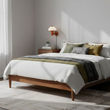 Oak wall lamp lit on a bedroom wall above a wood bed and green bedding