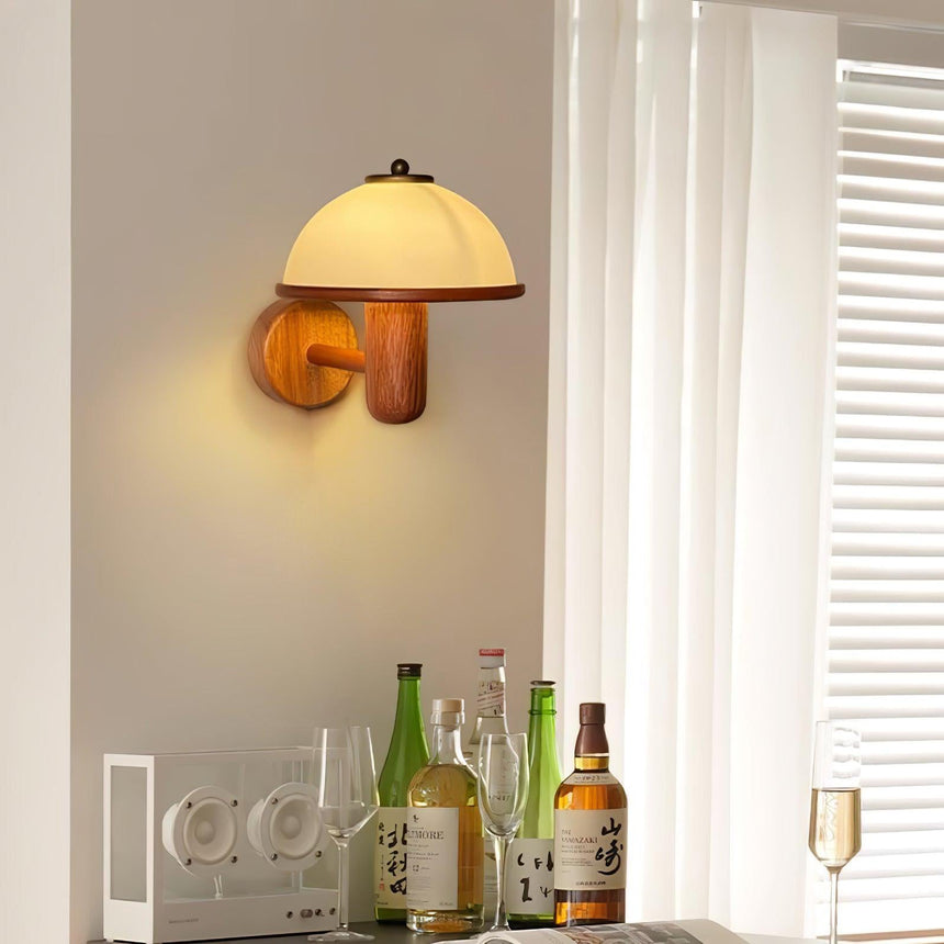 Oak wall lamp lit warm on a wall above bottles and a glass on a shelf