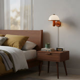 Oak wall lamp lit over a wood nightstand in a plain bedroom at night