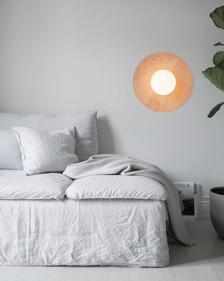 Lamp lit on a bedroom wall above a bed with a plant in the far corner