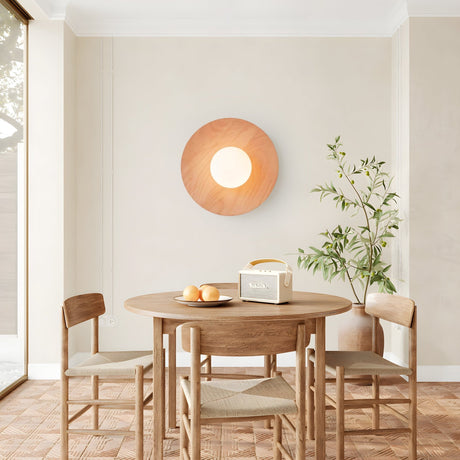 Lamp on a dining room wall beside a round table, chairs and an olive tree