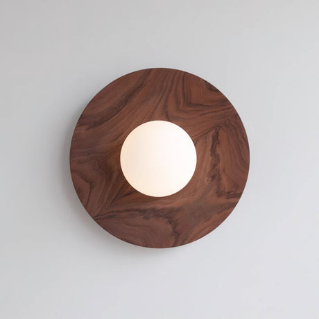 The largest walnut disc on a pale wall with the globe lit low and warm