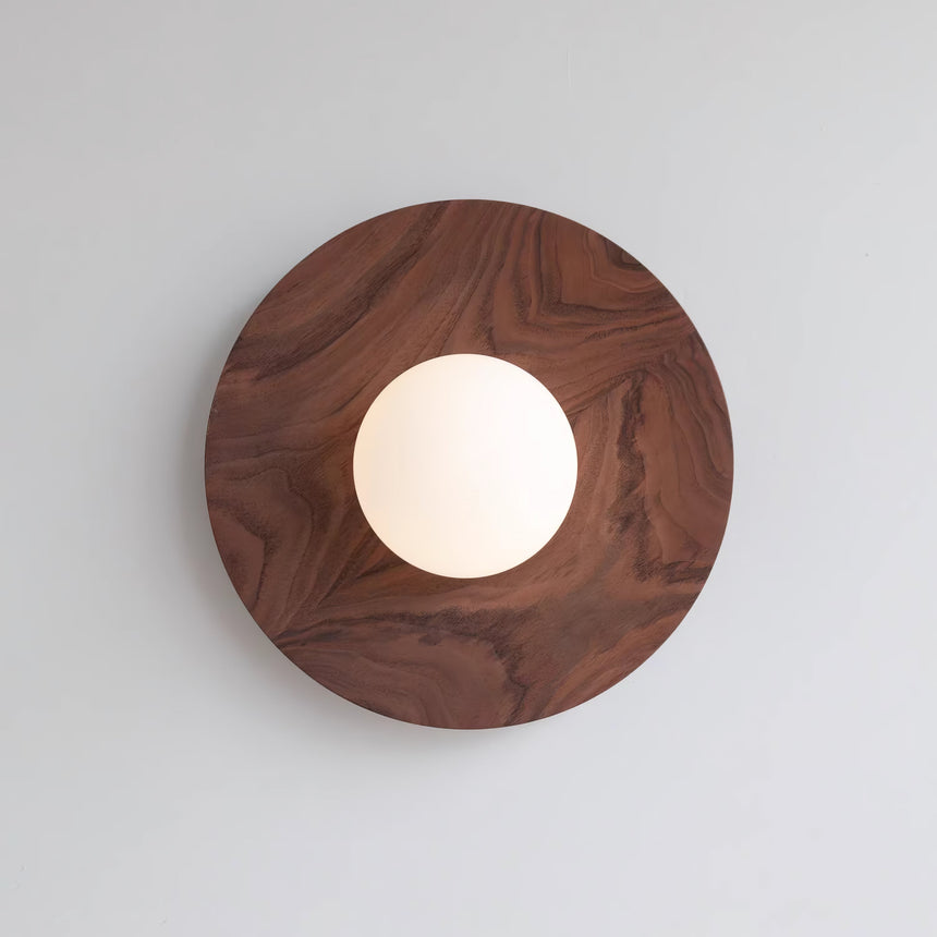 The largest walnut disc on a pale wall with the globe lit low and warm