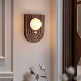 Alabaster orb lit warm on an arched walnut plate beside dried cotton stems