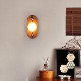 Alabaster sconce lit warm on a pale wall next to a wood blind and shelf
