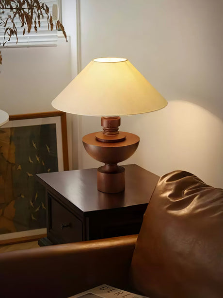 Black based beige table lamp lit on a table beside a leather chair