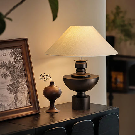 Black based beige table lamp lit on a sideboard beside a framed print