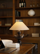 Beige table lamp lit on a desk in a room lined with wooden shelves
