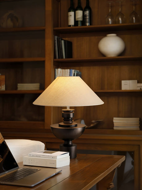 Beige table lamp lit on a desk in a room lined with wooden shelves
