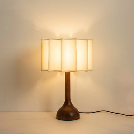 Beige table lamp lit warm against a plain wall, cord visible