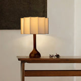 Beige table lamp lit on a narrow console table by a wall