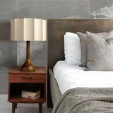 Beige table lamp lit on a nightstand beside a made bed