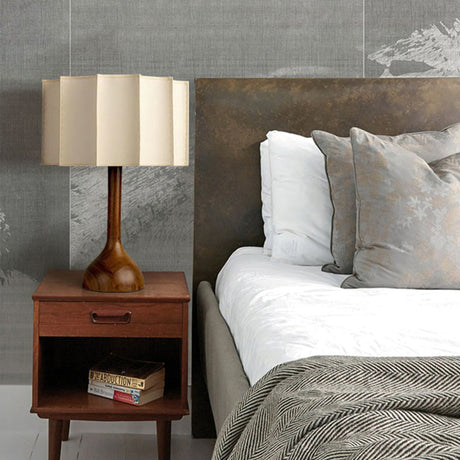 Beige table lamp lit on a nightstand beside a made bed