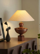 Beige table lamp lit on a sideboard in the corner of a pale room