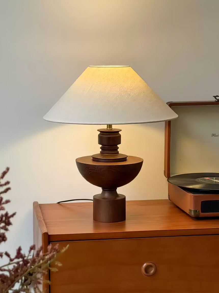 Beige table lamp lit on a wooden cabinet in front of a pale wall