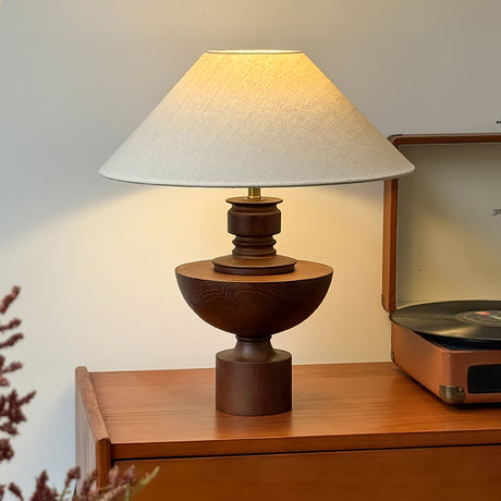 Beige table lamp lit on a wooden cabinet beside a record player