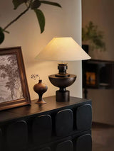 Beige table lamp lit on a sideboard beside a small dark vase