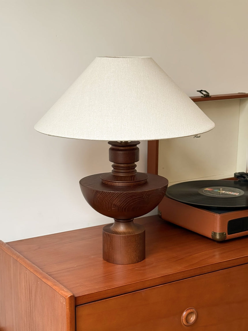 Beige table lamp lit on a wooden chest beside a record player