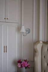 The sconce unlit above flowers beside a tufted headboard