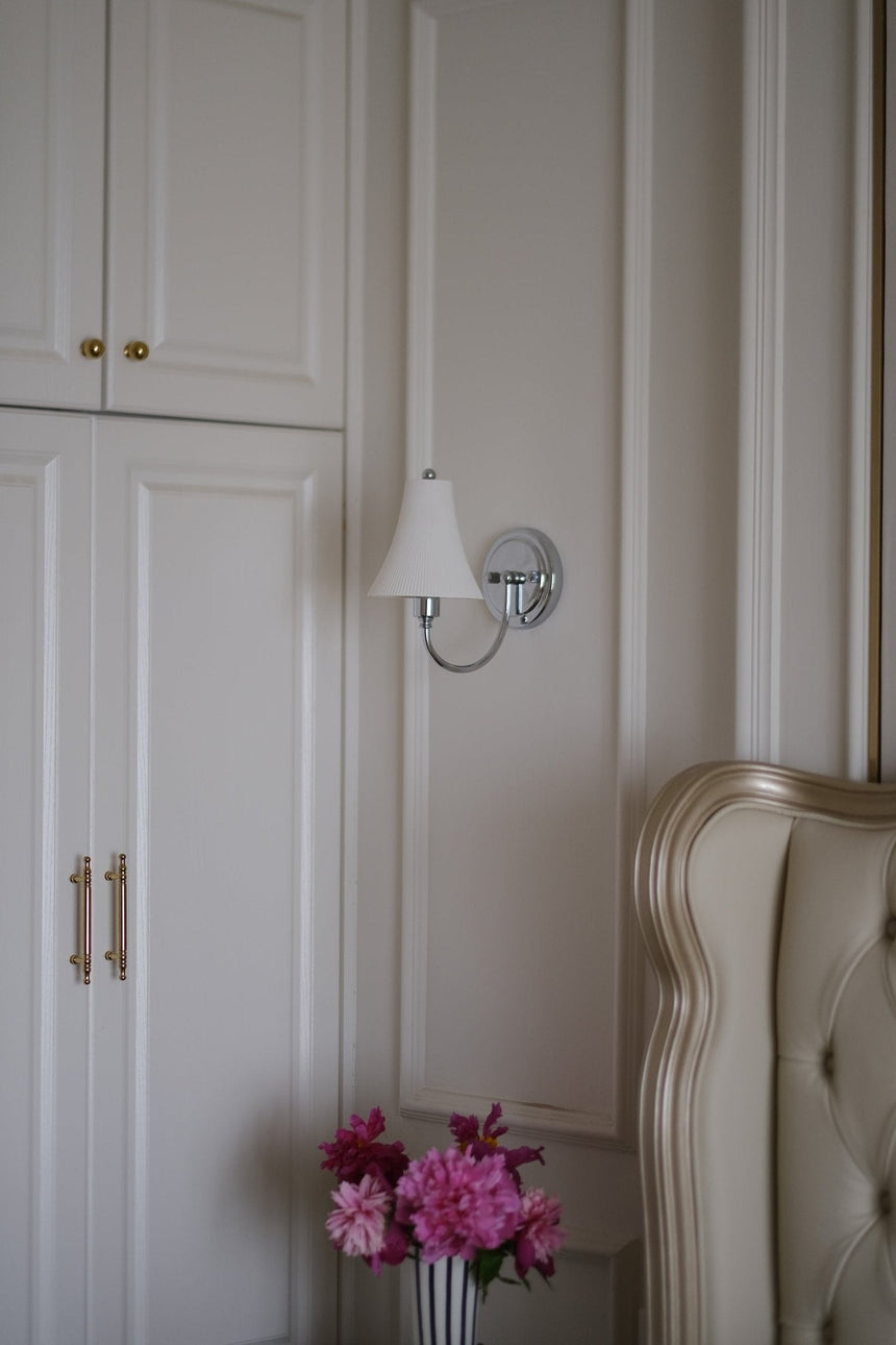 The sconce unlit above flowers beside a tufted headboard
