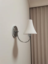 The sconce unlit beside a brown curtain, the chrome arm curving up