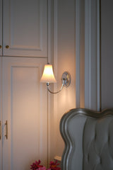 The sconce lit beside a tufted headboard, white wardrobe doors and pink flowers