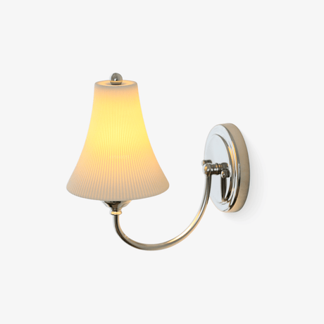 Chrome wall sconce with a curved arm and a white ribbed bell shaped ceramic shade, lit