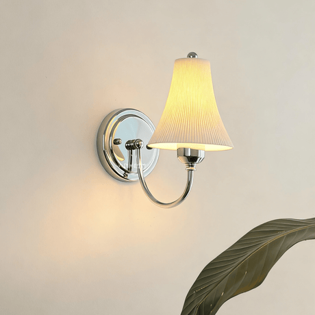 The bell shade lit on a warm white wall behind large green leaves