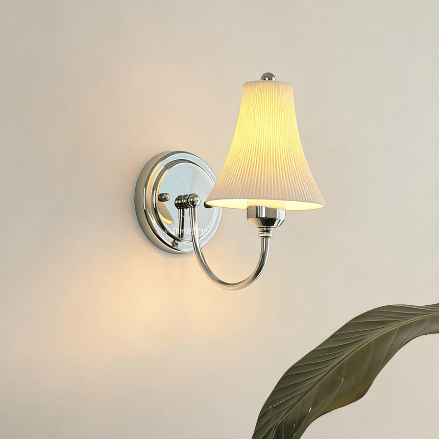 The bell shade lit on a warm white wall behind large green leaves