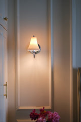 The sconce lit on a paneled wall between white wardrobe doors, flowers below
