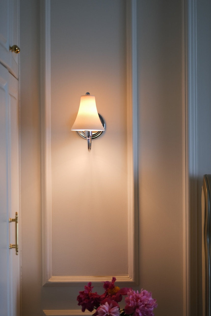 The sconce lit on a paneled wall between white wardrobe doors, flowers below